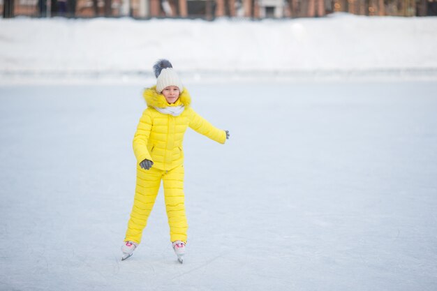 Entzückendes kleines Mädchen, das draußen auf die Eisbahn am warmen Wintertag eisläuft