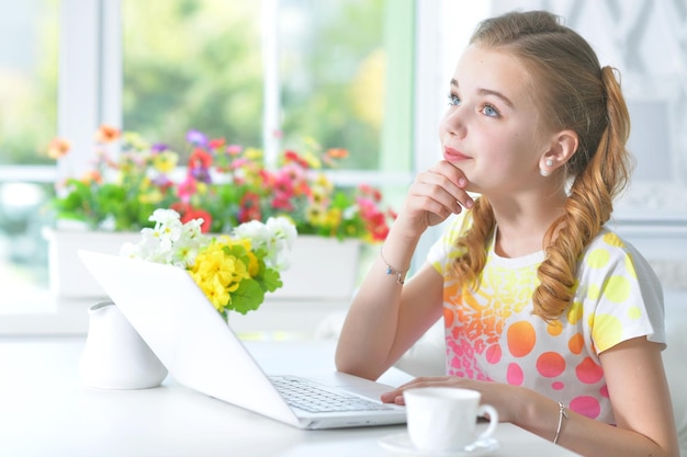 Entzückendes kleines Mädchen, das mit laptopc am Tisch sitzt