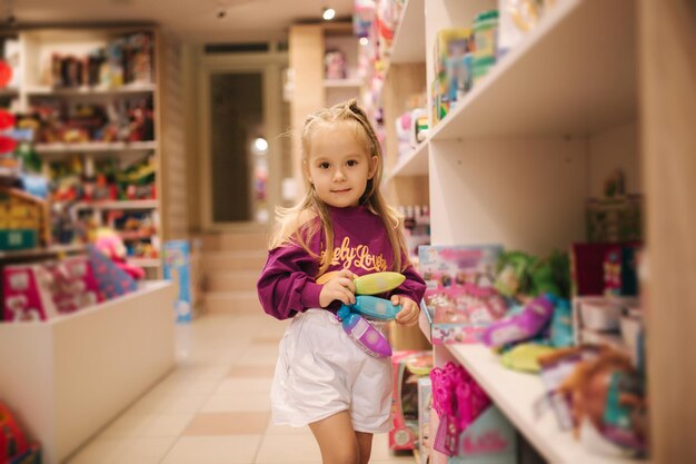 Entzückendes kleines mädchen, das spielzeug kauft, süße frau im spielzeugladen, glückliches junges mädchen, das spielzeug auswählt