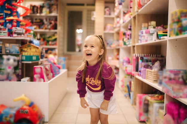 Foto entzückendes kleines mädchen, das spielzeug kauft, süße frau im spielzeugladen, glückliches junges mädchen, das spielzeug auswählt