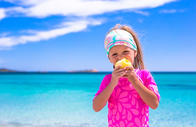 Entzückendes kleines Mädchen essen Apfel am tropischen Strand während der Ferien