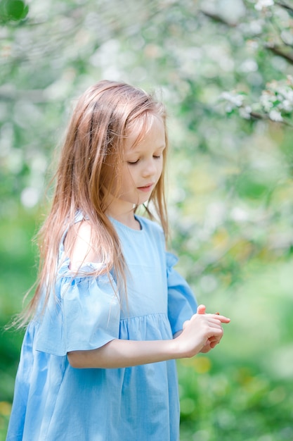 Entzückendes kleines Mädchen in blühendem Apfelgarten am schönen Frühlingstag