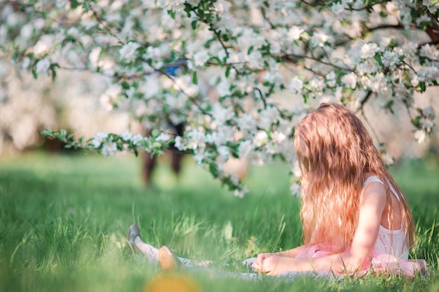 Entzückendes kleines Mädchen in blühendem Kirschbaumgarten am Frühlingstag