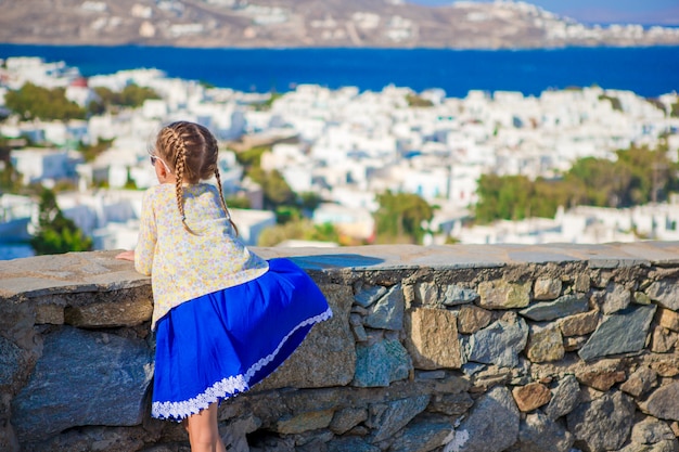 Entzückendes kleines Mädchen in der erstaunlichen Ansicht des Mykonos-Stadthintergrundes von traditionellen weißen Häusern