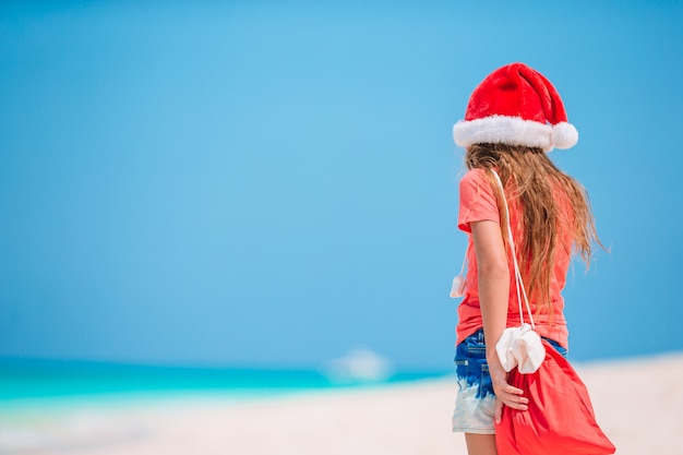 Entzückendes kleines Mädchen in der Weihnachtsmütze am tropischen Strand