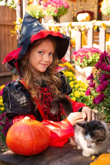 Entzückendes kleines Mädchen mit Halloween-Kostüm, das Spaß auf einem Kürbisbeet an einem schönen Herbsttag hat