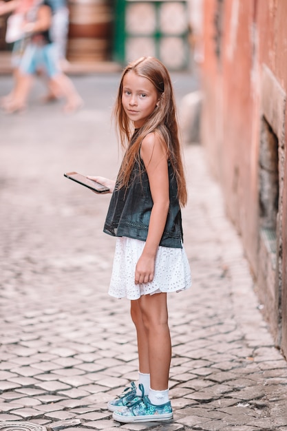 Foto entzückendes kleines mädchen mit handy an der italienischen stadt während der sommerferien