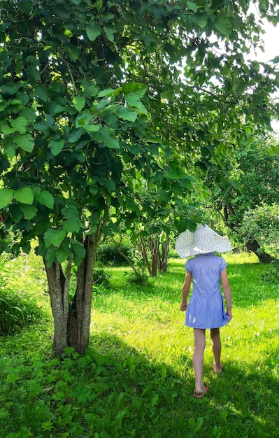 Entzückendes kleines Mädchen mit weißem Hut, das in einem Sommerpark spazieren geht