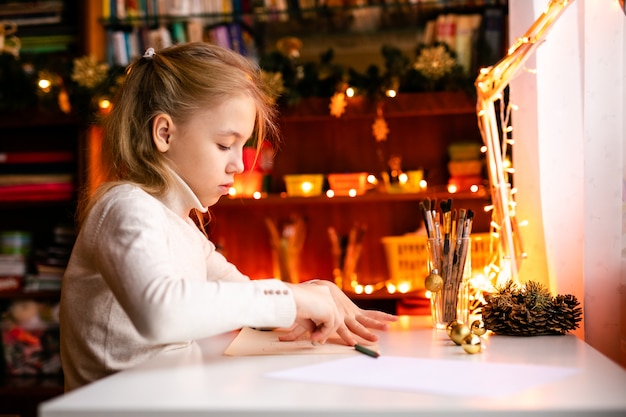 Entzückendes kleines Mädchen schreibt Santa Klaus einen Brief, der auf dem Tisch sitzt