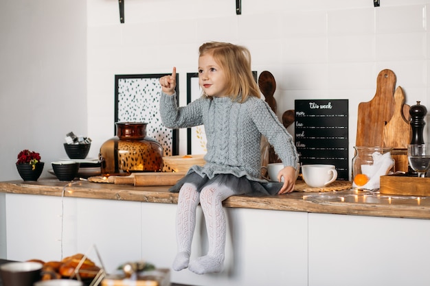 Entzückendes kleines Mädchen sitzt auf Küchentisch. Kleines Mädchen in der Küche zu Hause