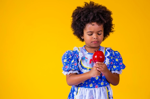 Entzückendes kleines schwarzes Mädchen in Juni-Partykleidung, das Love Apple isst Apfeldessert mit rotem Karamell bedeckt