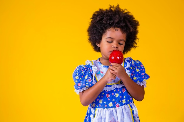 Entzückendes kleines schwarzes Mädchen in Juni-Partykleidung, das Love Apple isst Apfeldessert mit rotem Karamell bedeckt