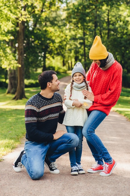 Entzückendes kleines süßes Kind, das froh ist, von den Eltern unterstützt zu werden, teilt ihre Gefühle nach dem Besuch des Kindergartens und hat eine gute Entspannung im Park Modellfamilienspaziergänge im Park haben fröhliche Ausdrücke