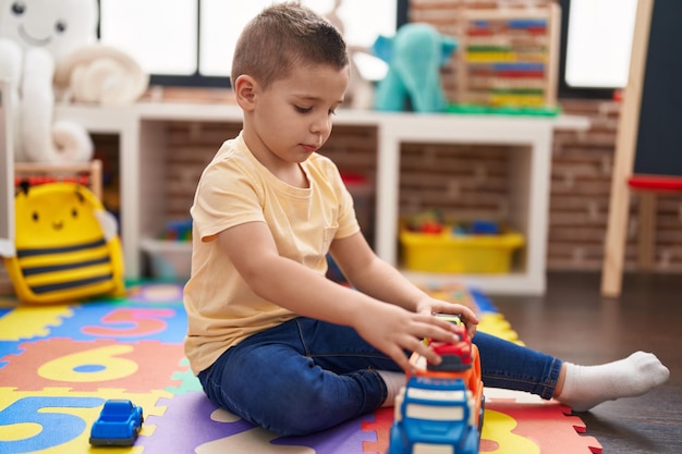 Entzückendes Kleinkind, das mit Autospielzeug spielt, das im Kindergarten auf dem Boden sitzt