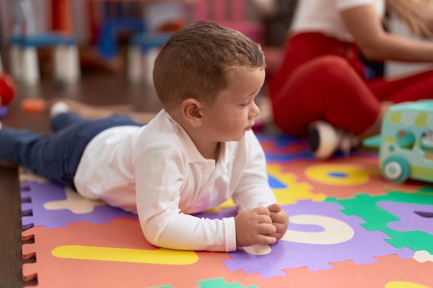 Entzückendes Kleinkind, das mit entspanntem Gesichtsausdruck im Kindergarten auf dem Boden liegt