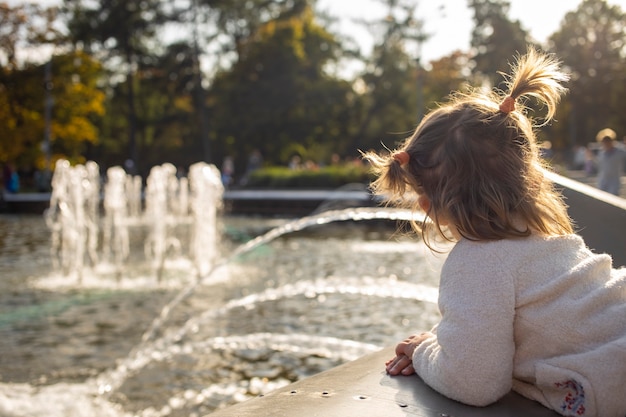 Entzückendes Kleinkindmädchen betrachtet die Brunnen im Park im Park an einem sonnigen Tag