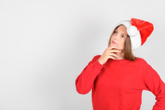 Entzückendes lächelndes Mädchen mit rotem Hut des Weihnachtsmanns, der roten Pullover trägt