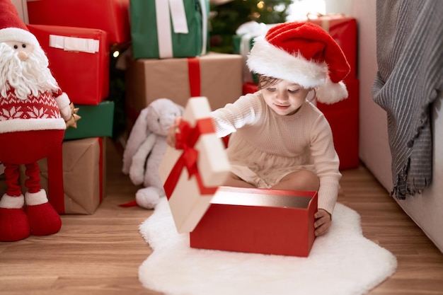 Entzückendes Mädchen, das Geschenk auspackt, das zu Hause am Weihnachtsbaum sitzt