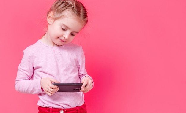 Entzückendes Mädchen, das Smartphone über rosa Hintergrund verwendet