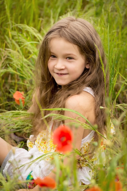 Entzückendes Mädchen im Alter von 6 Jahren in einem hellen Mohnfeld Porträt eines süßen Mädchens mit langen lockigen Haaren vor einem Sommerfeld voller roter Mohnblumen