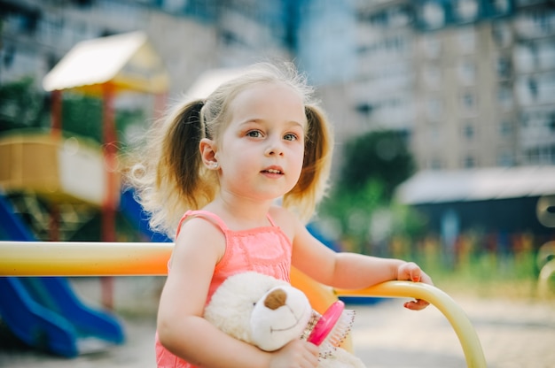 Entzückendes Mädchen im Kleid schwingen auf Spielplatz im Park. Kleines Mädchen im Kleid auf dem Spielplatz im Sommer