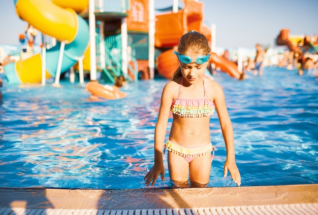 Entzückendes Mädchen in Schutzbrille zum Schwimmen im Pool stehen und Streusel, die ihre Hände hochhebt