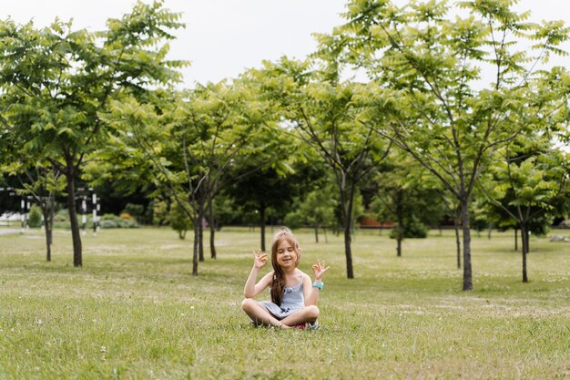 Foto entzückendes mädchen sitzt und meditiert in lotus-pose im park entspannung und meditation von kindern im freien lebensstil eines ruhigen kleinkindes genießen sie das leben