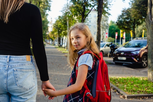 Entzückendes süßes kleines Mädchen, das aufgeregt ist, mit ihrer Mutter an der Hand von der Schule zurück zu gehen