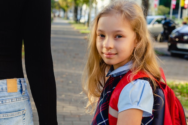 Entzückendes süßes kleines Mädchen, das aufgeregt ist, mit ihrer Mutter an der Hand von der Schule zurück zu gehen