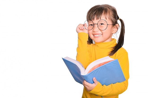 Entzückendes und fröhliches asiatisches kleines Mädchen, das eine Brille trägt, die interessantes Buch liest, das an der Bildung beteiligt ist, die auf Weiß isoliert wird