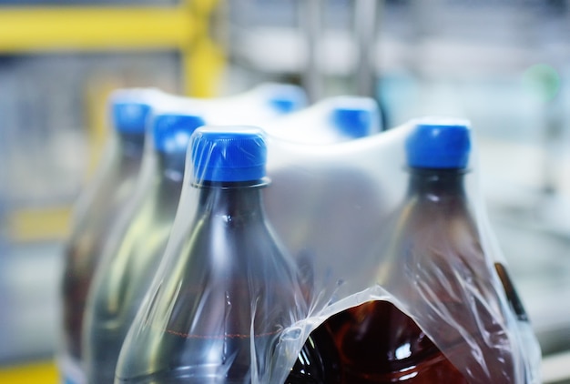 Envasado de botellas de plástico PET con cerveza o líquido en tetra pack de polietileno. Producción industrial de bebidas.