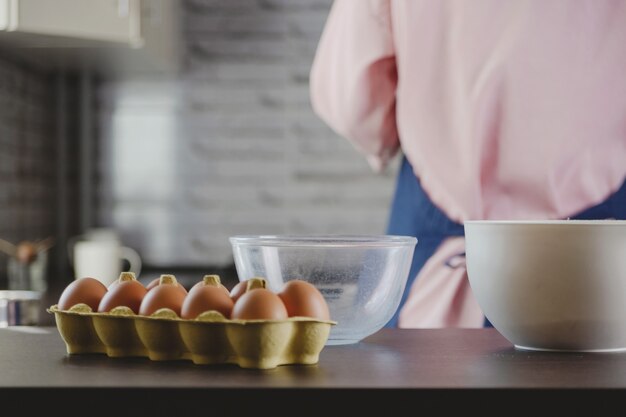 Envasado de huevos y tazones para hacer masa en el fondo de la cocina y la mujer que cocina en casa