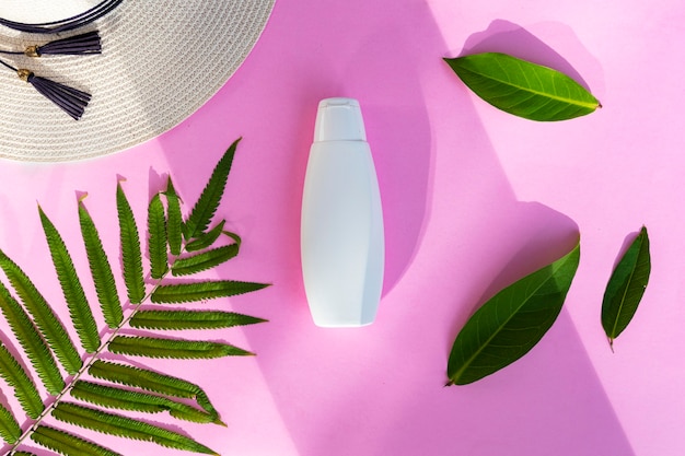 Envase botella cosmética blanca con hoja de palma y tapa blanca sobre fondo de papel rosa. Concepto de producto de belleza orgánica natural, estilo minimalista de verano.