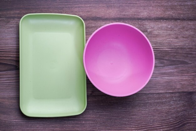 Los envases de alimentos hechos de plástico incluyen cuencos, platos y platos cuadrados en rosa y verde sobre madera