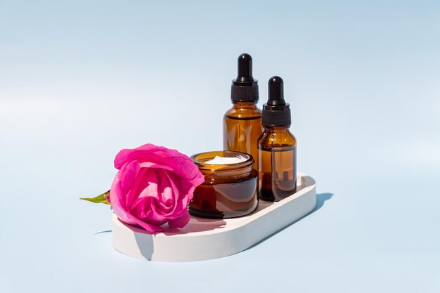 Envases cosméticos con rosa rosa Conjunto de diferentes botellas cosméticas de crema o suero sobre fondo azul Envases en blanco Concepto de producto de spa de belleza natural Mockup