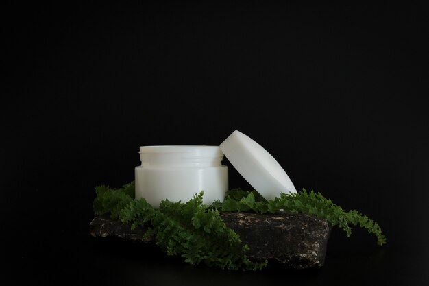 Envases de crema cosmética natural sin marca de pie en el podio de piedra. Presentación crema sobre fondo negro. Bosquejo. Concepto de tendencia en materiales naturales. Cosmética natural, cuidado de la piel.