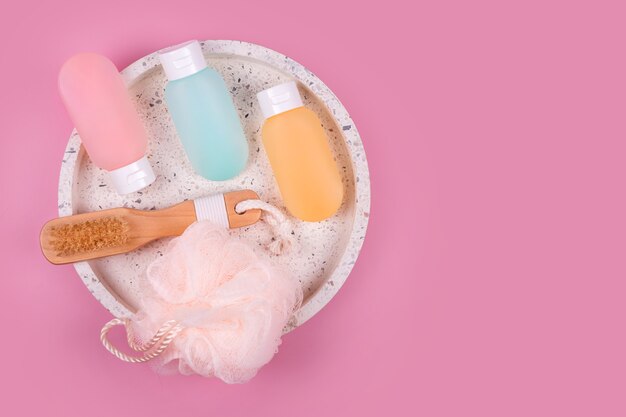 Envases de plástico de colores para champú, bálsamo para el cabello y gel de ducha con paños en una bandeja de mármol. Productos cosméticos para accesorios de spa y baño sobre fondo rosa