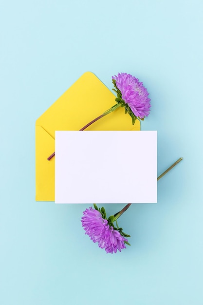 Envelope amarelo de cartão em branco branco e flor roxa em fundo azul estilo mínimo vista superior maquete plana