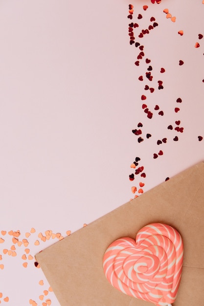 Envelope artesanal ao lado de corações de caramelo e uma cesta de vime em cores rosa pastel. Plano de fundo dia dos namorados.