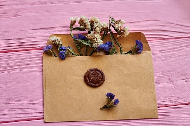 Envelope bege com flores na mesa de madeira rosa anexado selo marrom