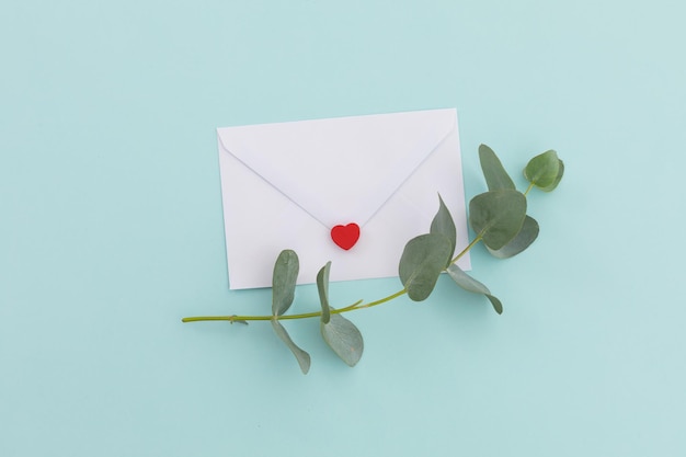 Foto envelope branco com coração e galho e folhas sobre fundo azul claro. amor romance dia dos namorados saudações mensagem carta cópia espaço.