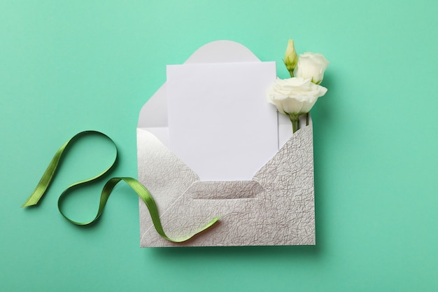 Envelope com cartão em branco, rosas e fita verde em fundo de hortelã