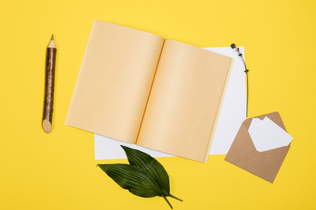 envelope com lençóis brancos, caderno aberto e lápis mentem sobre um fundo amarelo