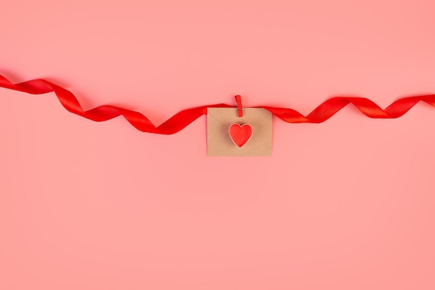 Envelope de artesanato com coração vermelho ligado a uma fita vermelha giratória em fundo rosa Amor romântico