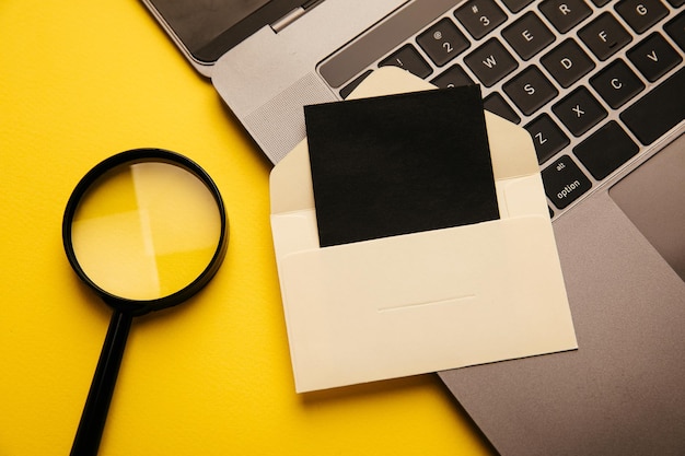 Foto envelope de papel com lupa de cartão e laptop em um fundo amarelo vista superior