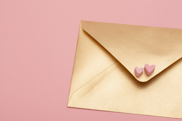 Foto envelope de papel dourado com dois corações de marshmallow isolado em fundo rosa