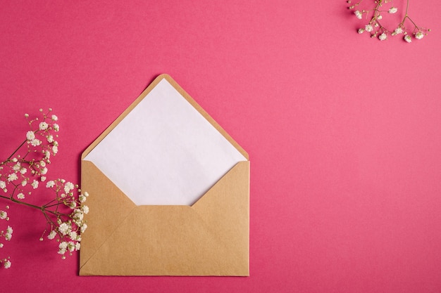 Envelope de papel kraft marrom com cartão branco vazio, flores gypsophila, fundo rosa vermelho, modelo de maquete