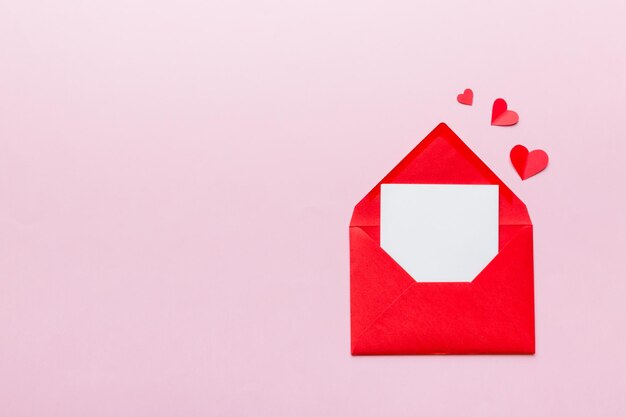 Envelope de papel vermelho com cartão branco vazio e coração no conceito de dia dos namorados de vista superior de fundo colorido