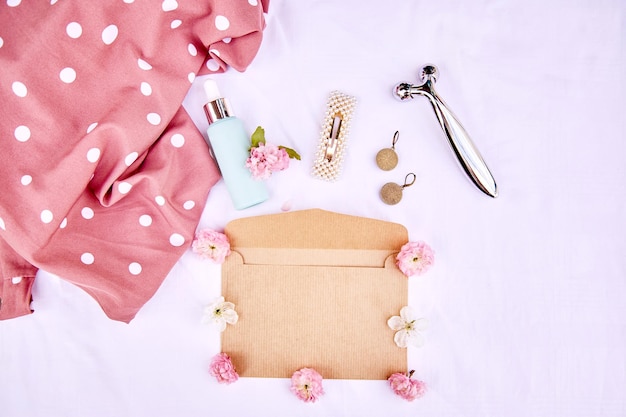 Envelope elegante de primavera vívido simulado com acessórios de flores rosa massageador presente cosmético em tecido branco de fundo 8 de março conceito