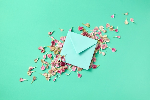 envelope feito à mão com pétalas de flores sobre fundo claro turquesa e lugar para texto. Postura plana. Cartão de felicitações.